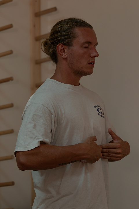 A young man in light-colored clothing meditates, practicing self-analysis and self-awareness.