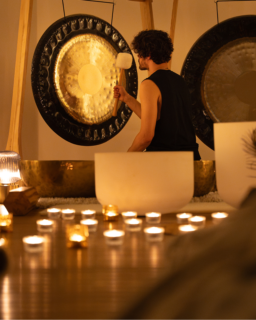 Relaxation and meditation: a woman relaxes on a mat in a sound therapy studio with lit candles, large gongs, and crystal singing bowls.
