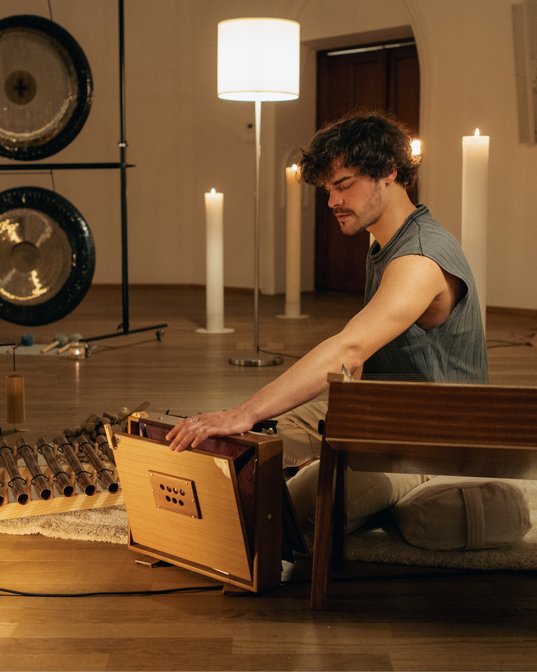 Relaxation and meditation: a woman relaxes on a mat in a sound therapy studio with lit candles, large gongs, and crystal singing bowls.